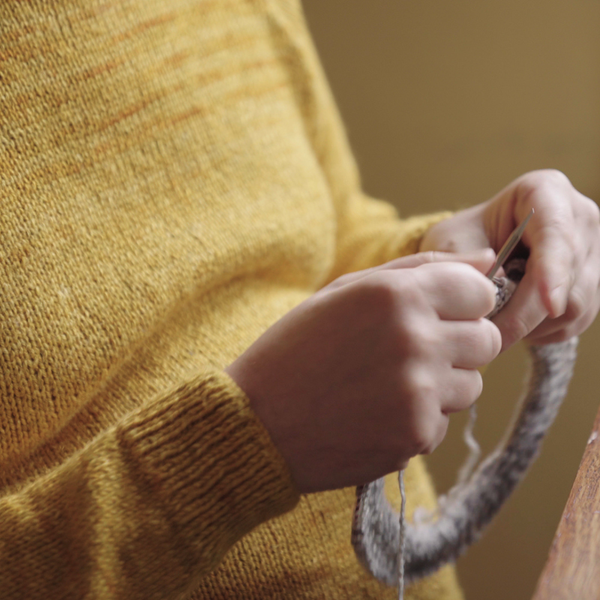 man knitting in the round wearing a yellow jumper