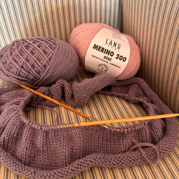 Knitting with Ball of MERINO 200 BÉBÉ yarn in soft pastel shade, showing smooth spin and fine texture